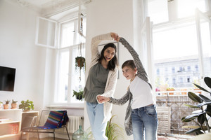 Mutter tanzt mit Tochter vergnügt durch Wohnzimmer, beide halten sich an der Hand