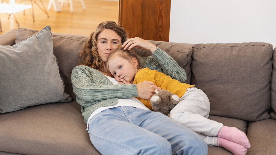Mother cuddling sick daughter on the couch