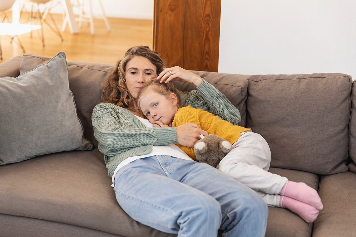 Kind erkältet: Was tun? 8 hilfreiche Tipps, die Ihrem Kind durch die Erkältung helfen Mutter kuschelt mit kranker Tochter auf der Couch