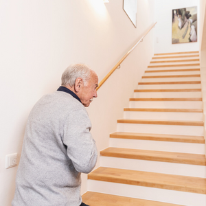 Älterer Mann steht an Fuß einer Treppe und hält sich die Brust