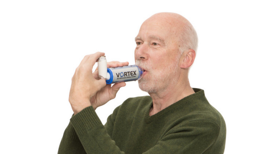 Mann inhaliert aus Asthmaspray mit Spacer