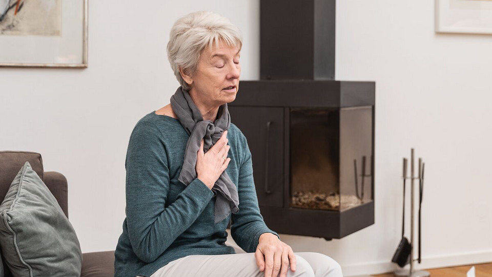 Flache Atmung als Atemtechnik gegen Hustenreiz: So geht’s Ältere Frau atmet auf der Couch sitzend flach ein, um Hustenreiz zu unterdrücken
