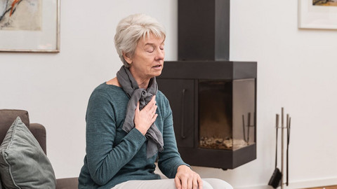 Flache Atmung als Atemtechnik gegen Hustenreiz: So geht’s Ältere Frau atmet auf der Couch sitzend flach ein, um Hustenreiz zu unterdrücken