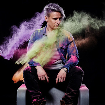 Young man sits on the back of a chair, colourful mist surrounds him