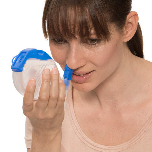 Woman holds nasal douche to her nose to rinse it