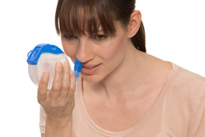 Frau hält sich Nasendusche an die Nase, um zu spülen