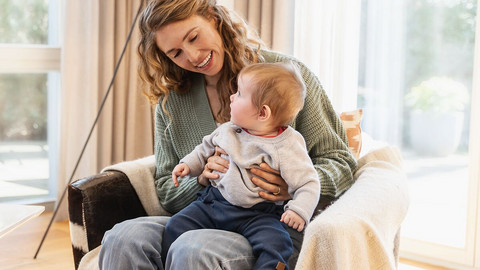 Mutter sitzt auf einem Sessel mit Baby auf dem Schoß, die beiden schauen sich an