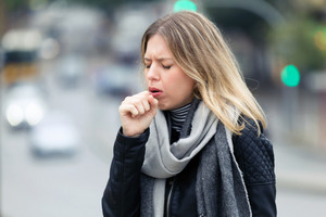 Woman with scarf holds hand over her mouth while coughing