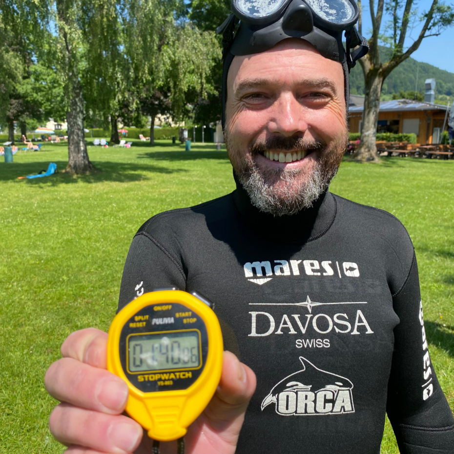 Taucher hält grinsend Stoppuhr in die Kamera