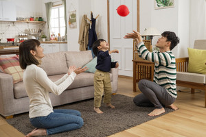 Mutter, Vater und kleiner Sohn spielen mit Luftballon am Boden im Wohnzimmer