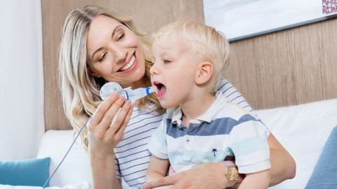 Junge Mutter hat kleinen Sohn auf dem Schoß und hilft ihm beim Inhalieren