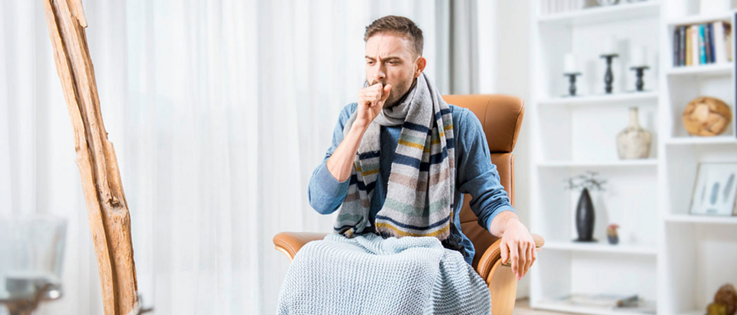 Man with cold and runny nose sits in a chair and coughs