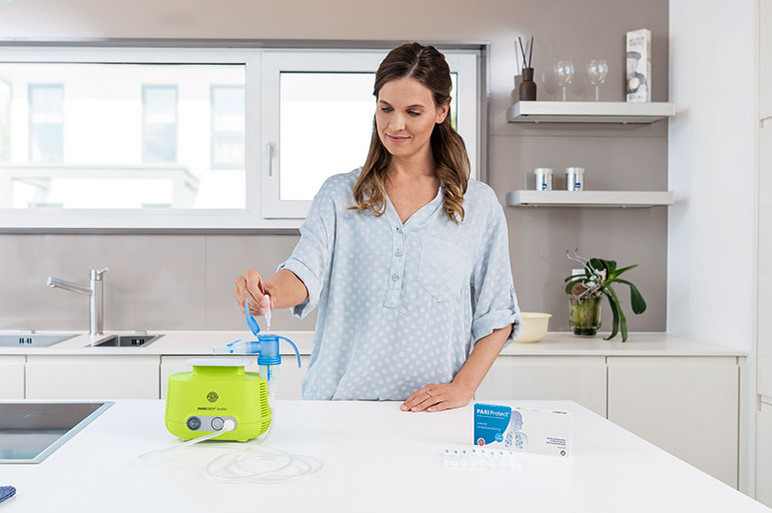 With inhalation for your airways Young woman in a bright kitchen filling a nebuliser attached to an inhalation device with saline solution.