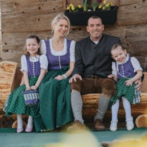 Mutter, Vater und zwei Töchter sitzen in Tracht auf einer Holzbank