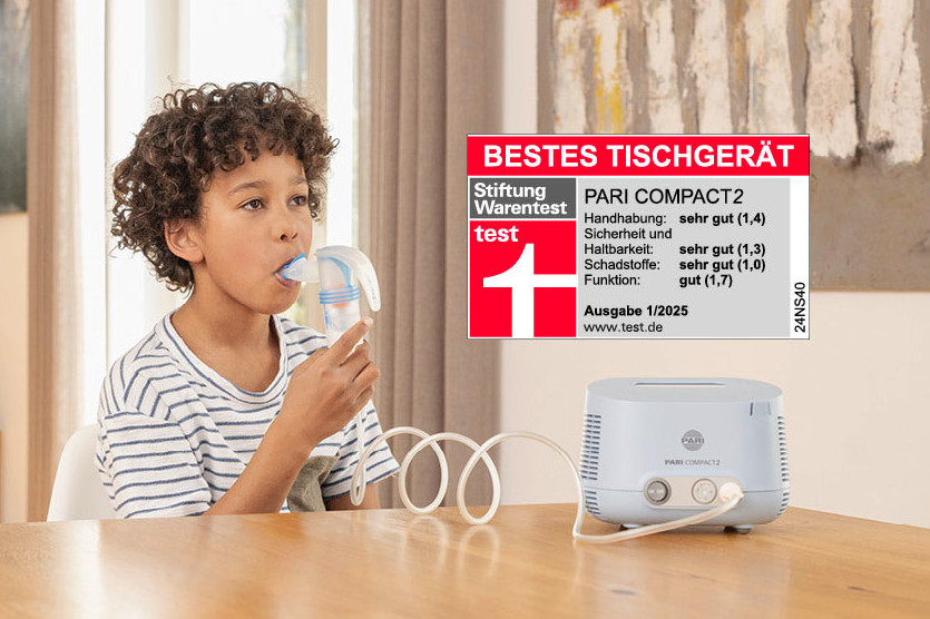 Ein Kind inhaliert mit einem blauen PARI COMPACT2 Inhalator, während der Vater unterstützend daneben sitzt.