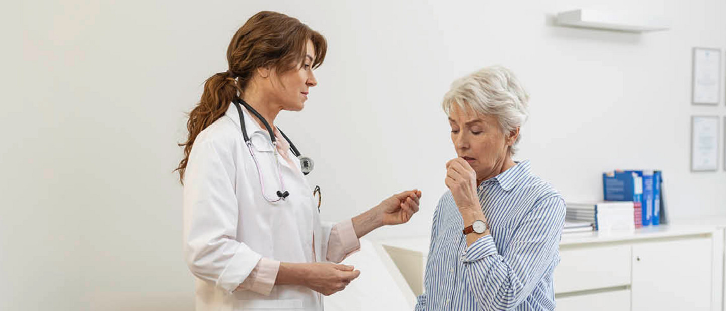 Different types of Coughs and treatments A doctor hands a medication to an elderly woman sitting on a couch in front of her. The woman holds her hand over her mouth and coughs.