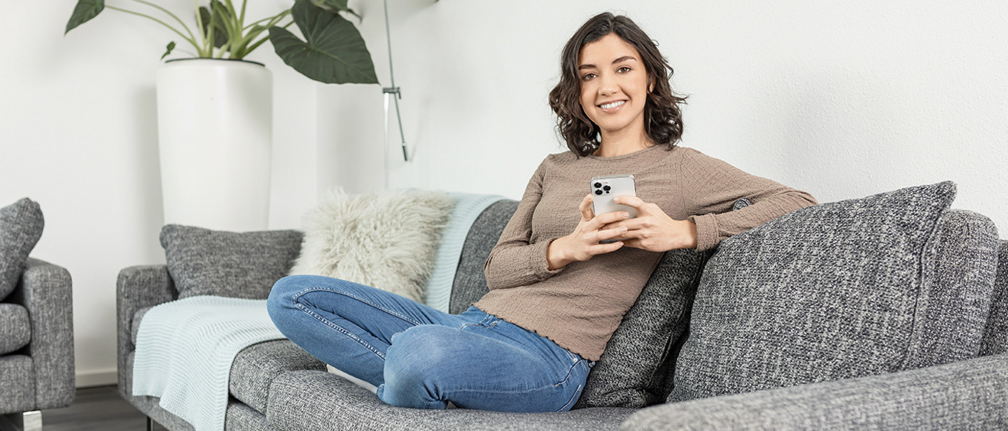 A person sits relaxed on the sofa, holding a smartphone and a cup in the living room.