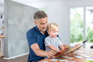 Vater sitzt mit Sohn am Tisch, ein Buch aufgeschlagen in der Hand