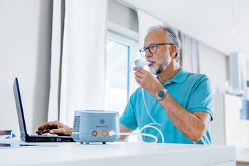 Mann inhaliert mit Inhaliergerät, während er am Laptop arbeitet