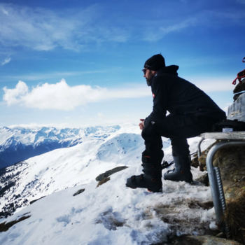 Mann sitzt auf einer Bank am Berg und schaut ins verschneite Tal
