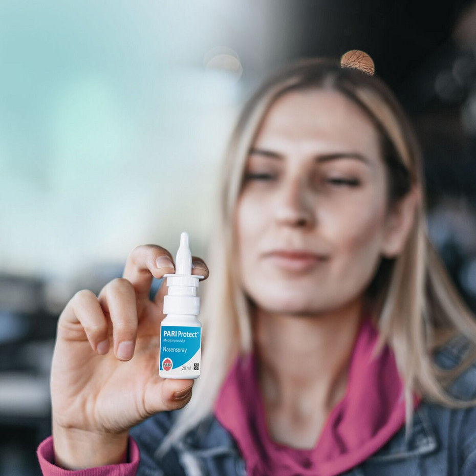 Frau hält PARI Protect Nasenspray in die Kamera