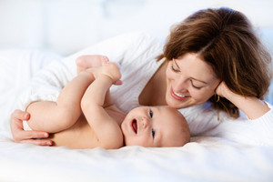 Mother lies on the bed with baby and watches it