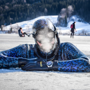 Nahaufnahme eines Tauchers, der aus einem Eisloch herausschaut, vor seinem Gesicht ist gefrierender Atem