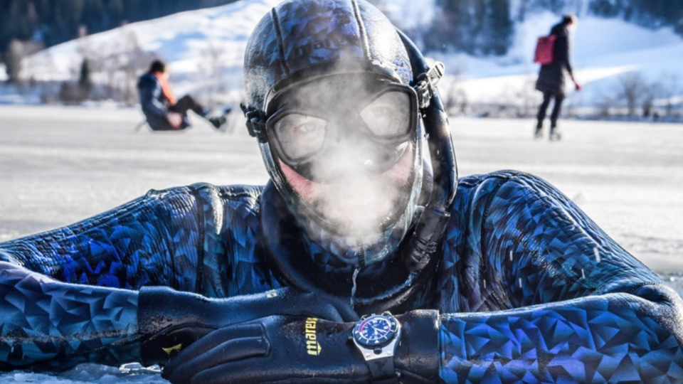 Nahaufnahme eines Tauchers, der aus einem Eisloch herausschaut, vor seinem Gesicht ist gefrierender Atem