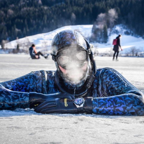 Nahaufnahme eines Tauchers, der aus einem Eisloch herausschaut, vor seinem Gesicht ist gefrierender Atem