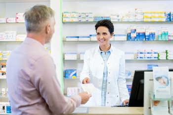 Elderly man standing in front of counter in pharmacy, pharmacist hands him a prescription