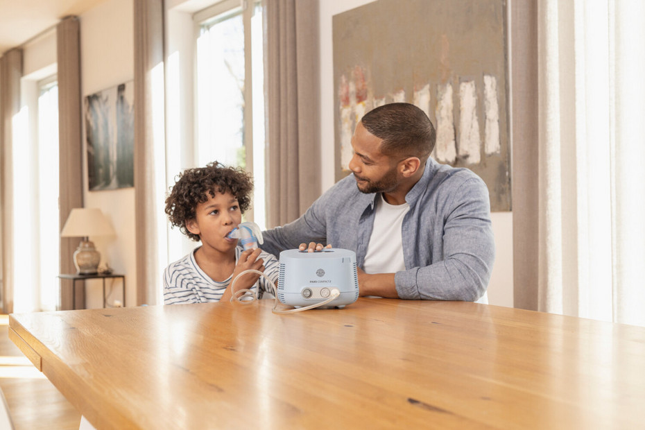 Frog in the throat: inhalation therapy Boy sitting at the table with his father, inhaling with the PARI COMPACT2 inhalation device