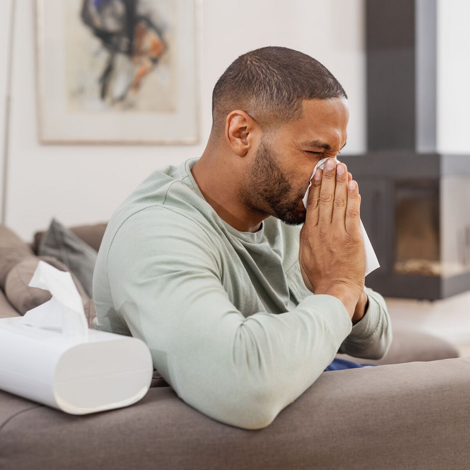 Young man sitting on the couch and blowing his nose