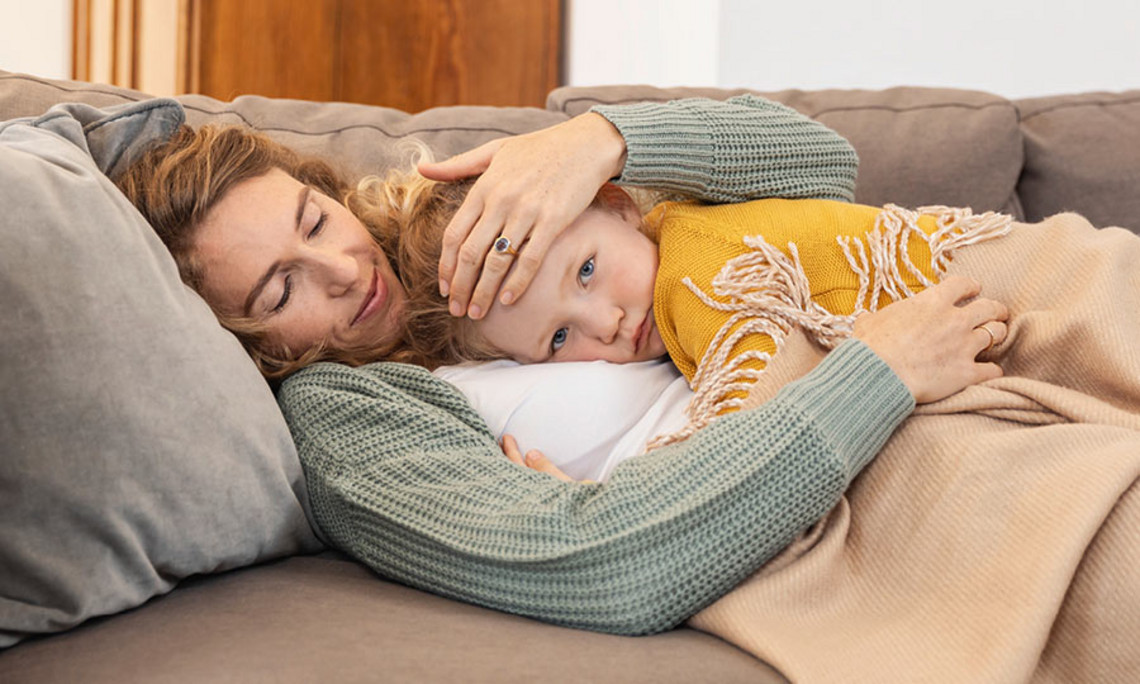 Mutter kümmert sich um ihr krankes Kind Mutter liegt auf einem Sofa und hält ihr Kind eng an sich, beide sind in eine Decke eingekuschelt.