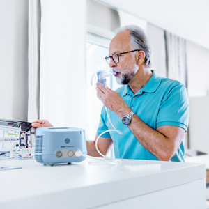 Älterer Mann liest in einer Zeitschrift, während er mit dem PARI COMPACT2 Inhalationsgerät inhaliert