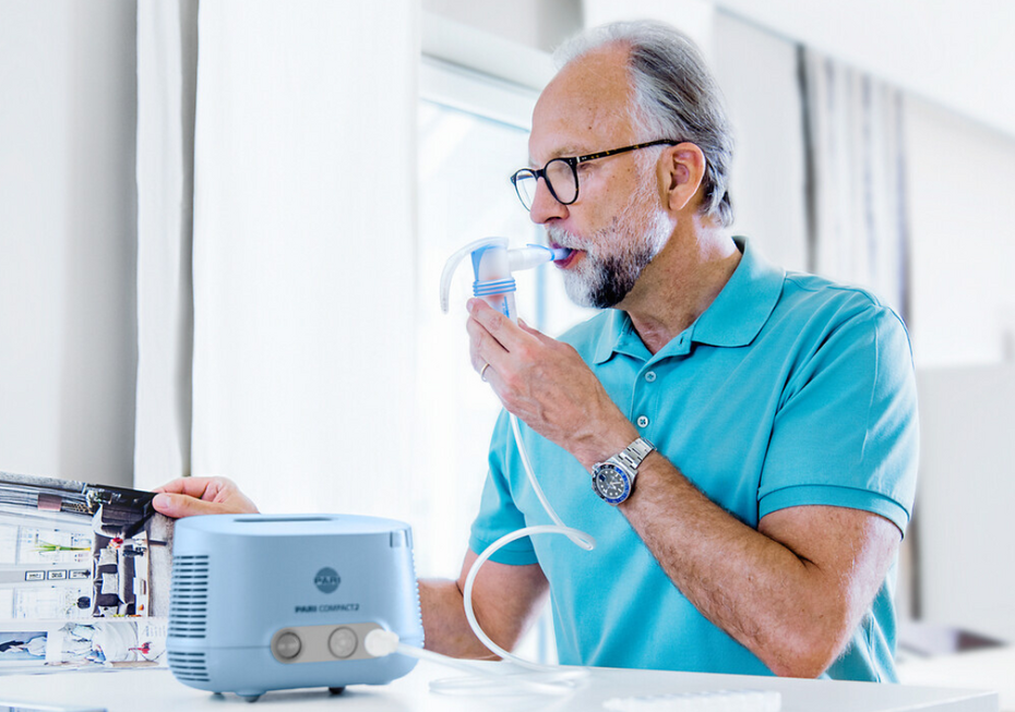 Älterer Mann liest in einer Zeitschrift, während er mit dem PARI COMPACT2 Inhalationsgerät inhaliert
