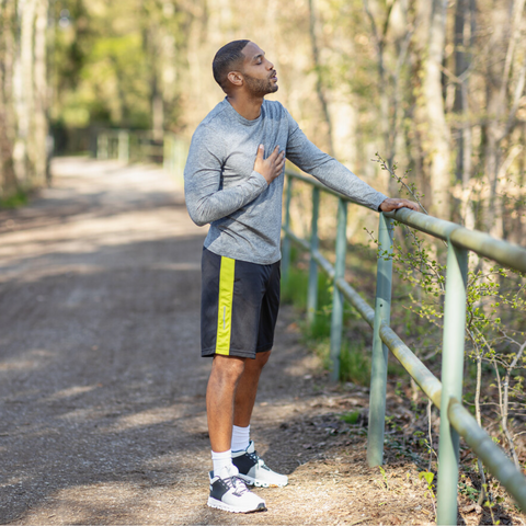 Jogger macht Pause, mit einer Hand hält er sich an einem Geländer fest, die andere liegt auf seiner Brust