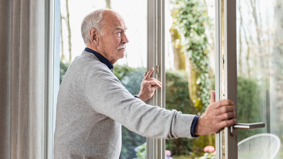 Älterer Mann steht an geöffnetem Fenster