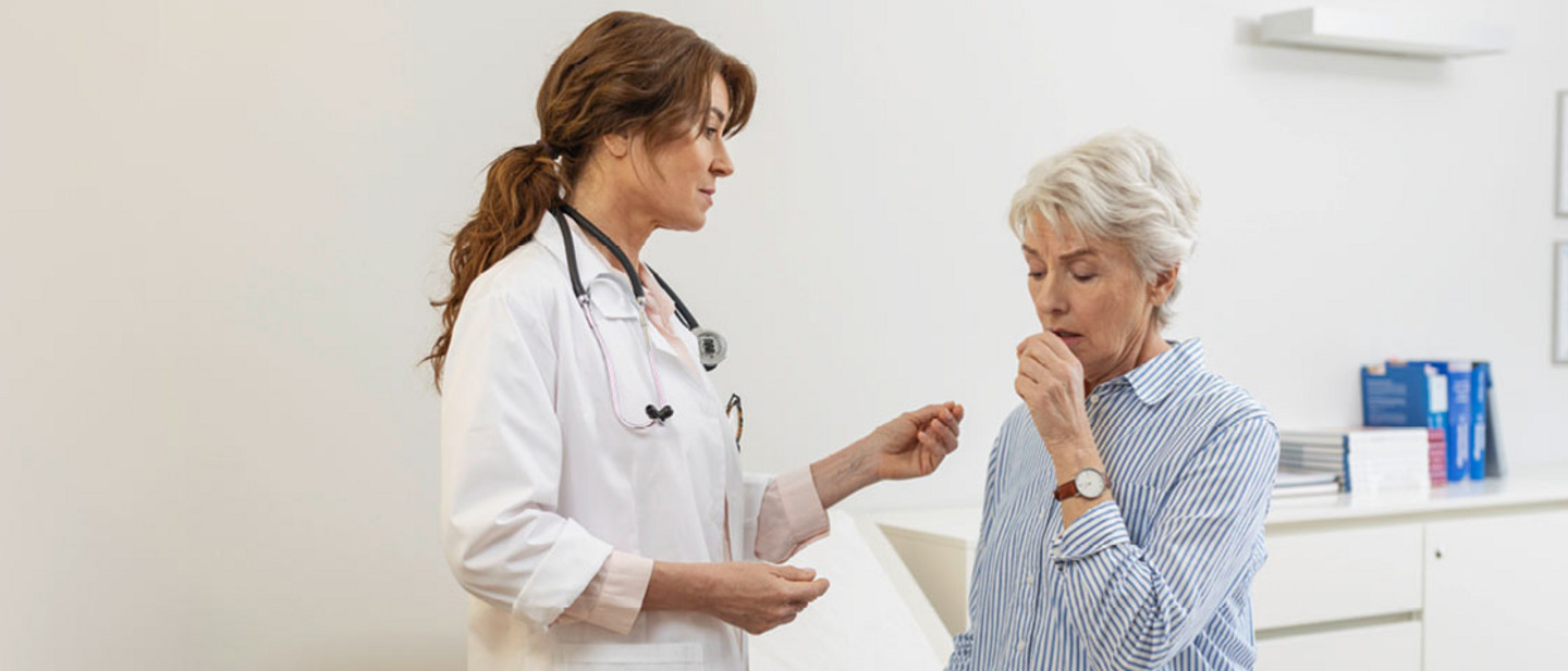 Doctor examining elderly woman with breathing difficulties in modern office, medical records and equipment in the background.