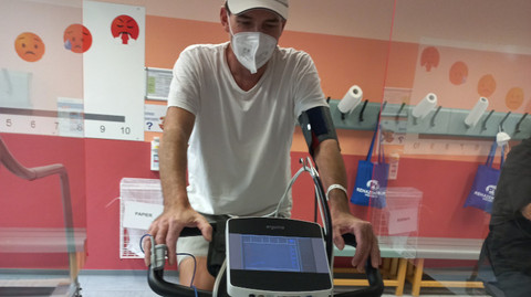 Mann sitzt mit Maske auf Hometrainer und trainiert
