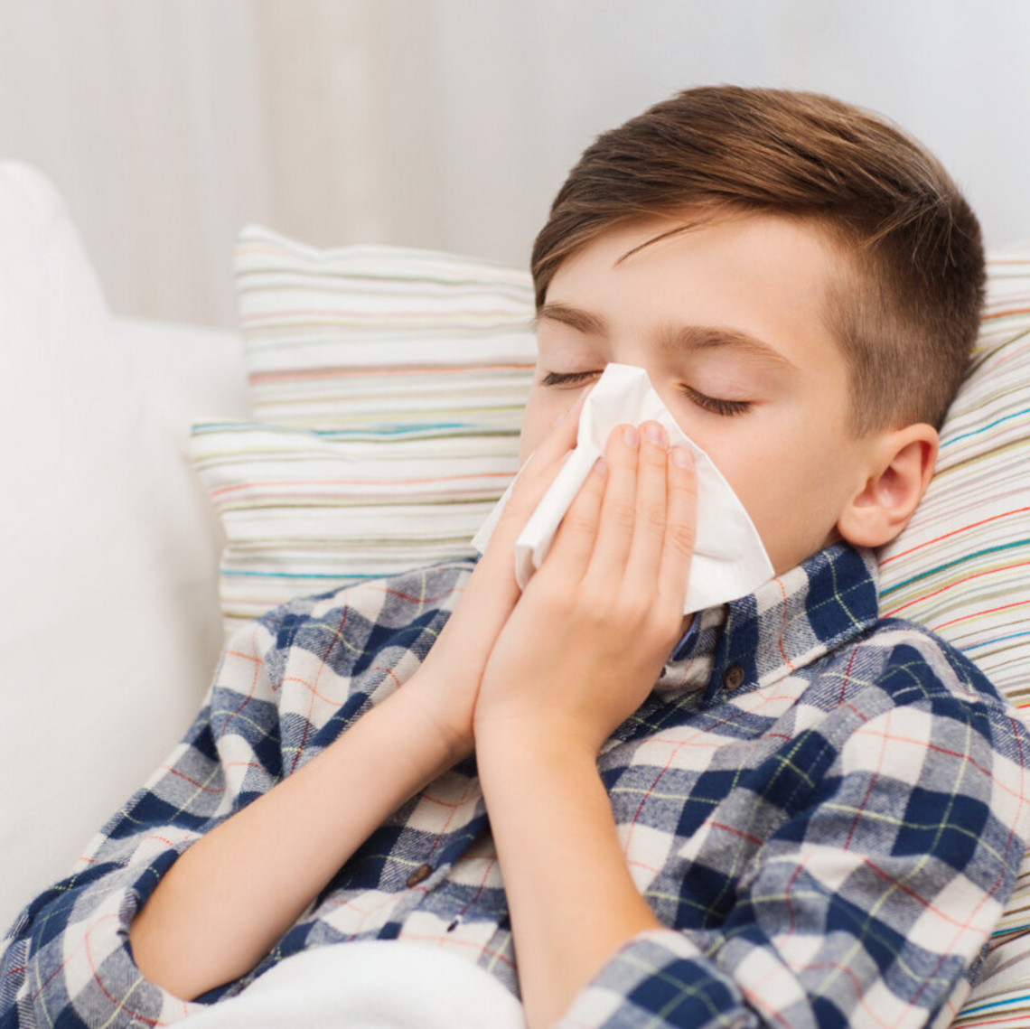 Junge in Halbnahaufnahme sitzt auf Couch und niest in ein Taschentuch