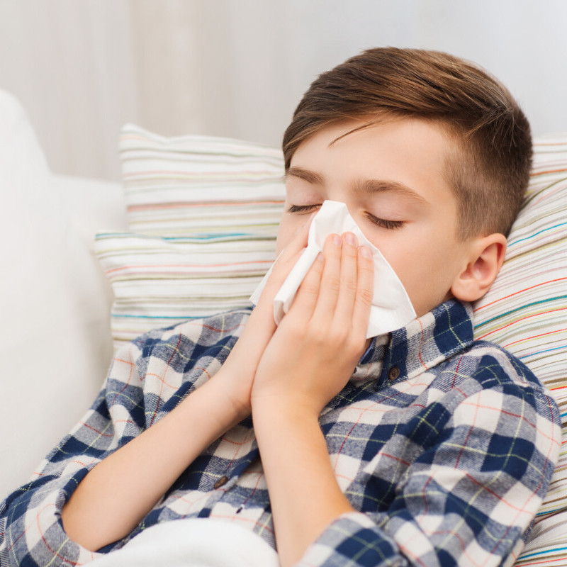 Asthma easy explanation for children: Allergy Boy in close-up sitting on a couch and sneezing into a handkerchief