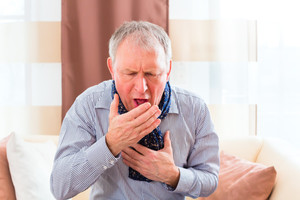 Coughing elderly man holds one hand to his chest, one in front of his mouth