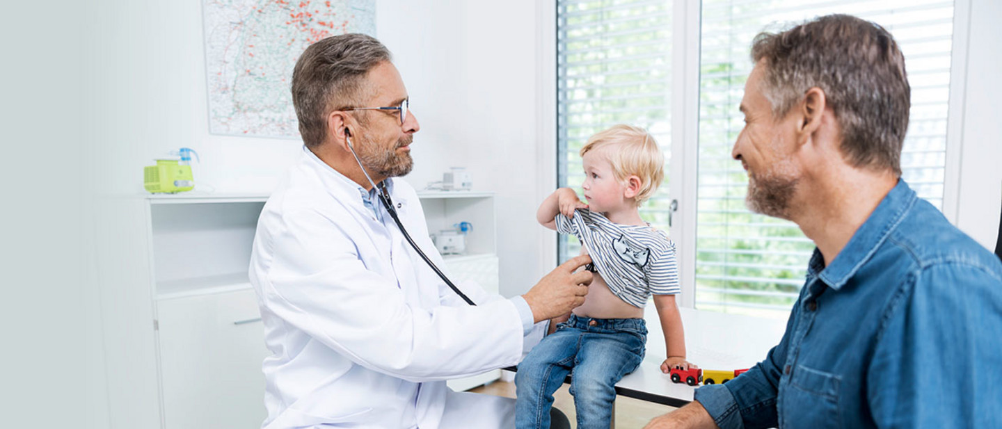 Behandlung von RS-Viren: Was die Inhalation mit Kochsalzlösung leisten kann Ein Arzt hört einen kleinen Jungen an der Brust ab, sein Vater sitzt daneben