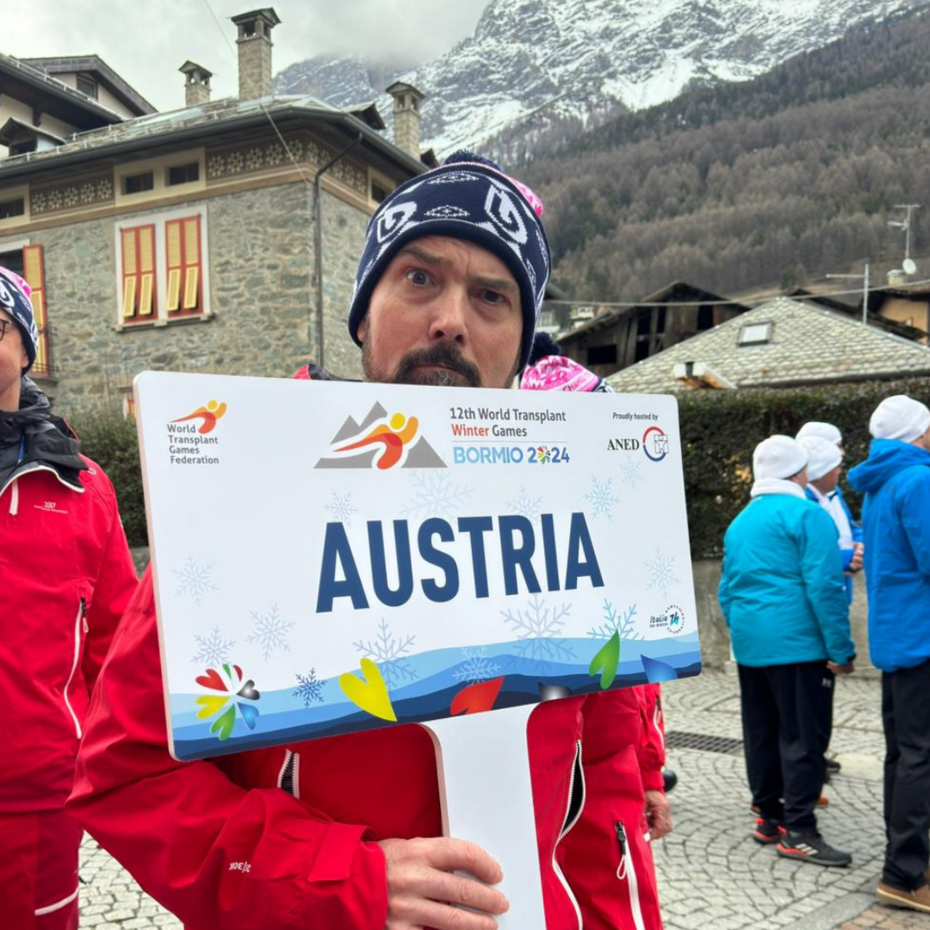 Bernhard Kaut auf dem Endspurt: World Transplant Winter Games Mann in Nahaufnahme, er hält ein Schild mit der Aufschrift Austria in der Hand