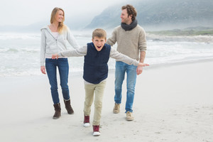 Mutter, Vater und Kind laufen am Strand entlang