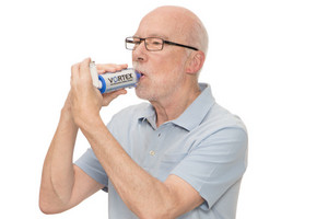 Älterer Mann mit Brille inhaliert Asthmaspray mit Hilfe eines Spacers