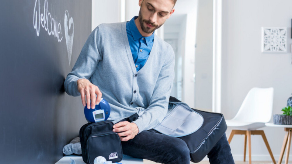 Young man sits on bench in aisle and puts inhalation device in bag