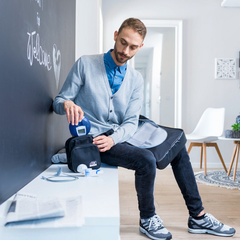 Junger Mann sitzt auf Bank im Gang und packt Inhalationsgerät in Tasche