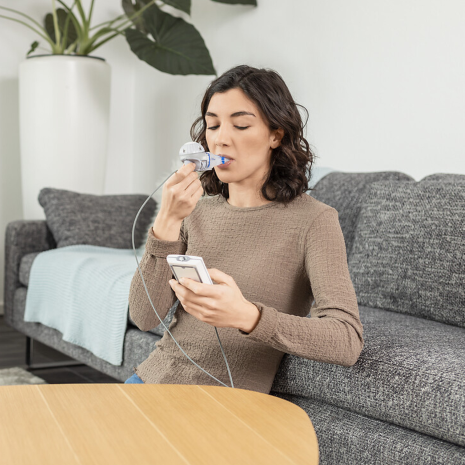 Junge Frau sitzt im Wohnzimmer und inhaliert mit dem eFlow®rapid