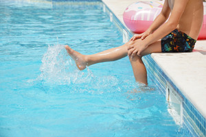 Junge sitzt am Beckenrand, die Beine im Wasser, Kopf ist nicht im Bild